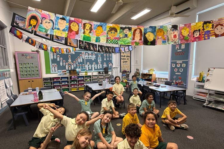 Photograph of a class sitting on the floor inside their classroom.